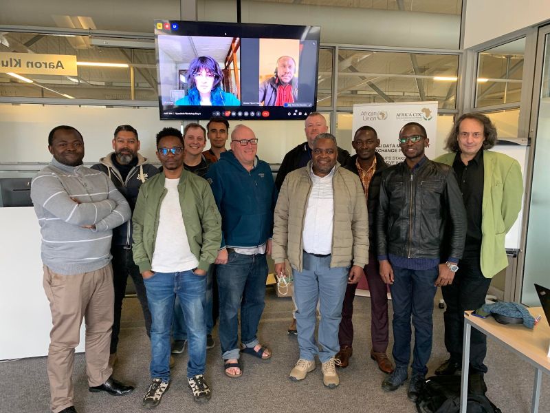 Workshop's participants standing in front of a monitor showing the two online participants